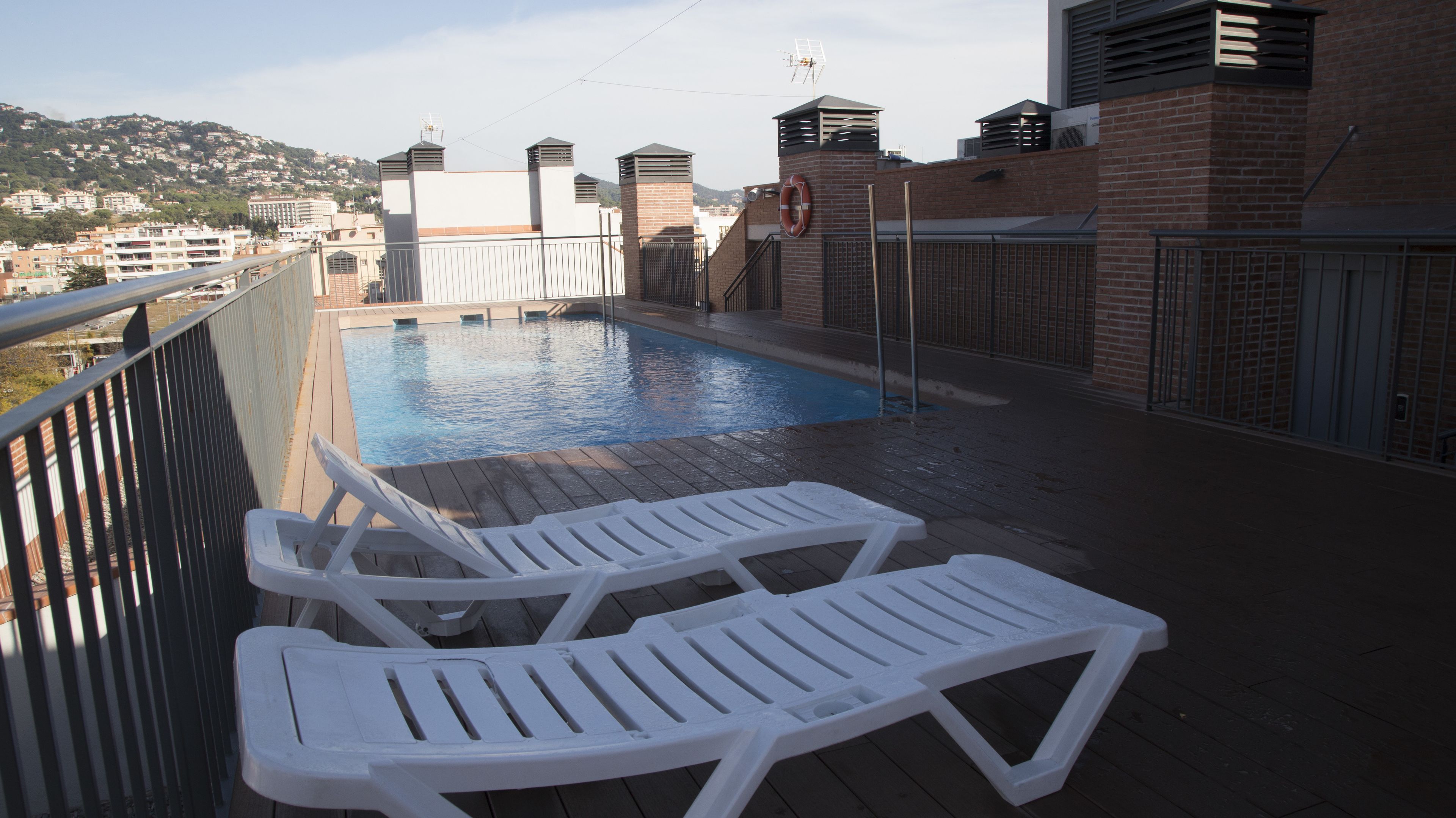 A rooftop pool area with two white lounge chairs and a view of the cityscape in the background.