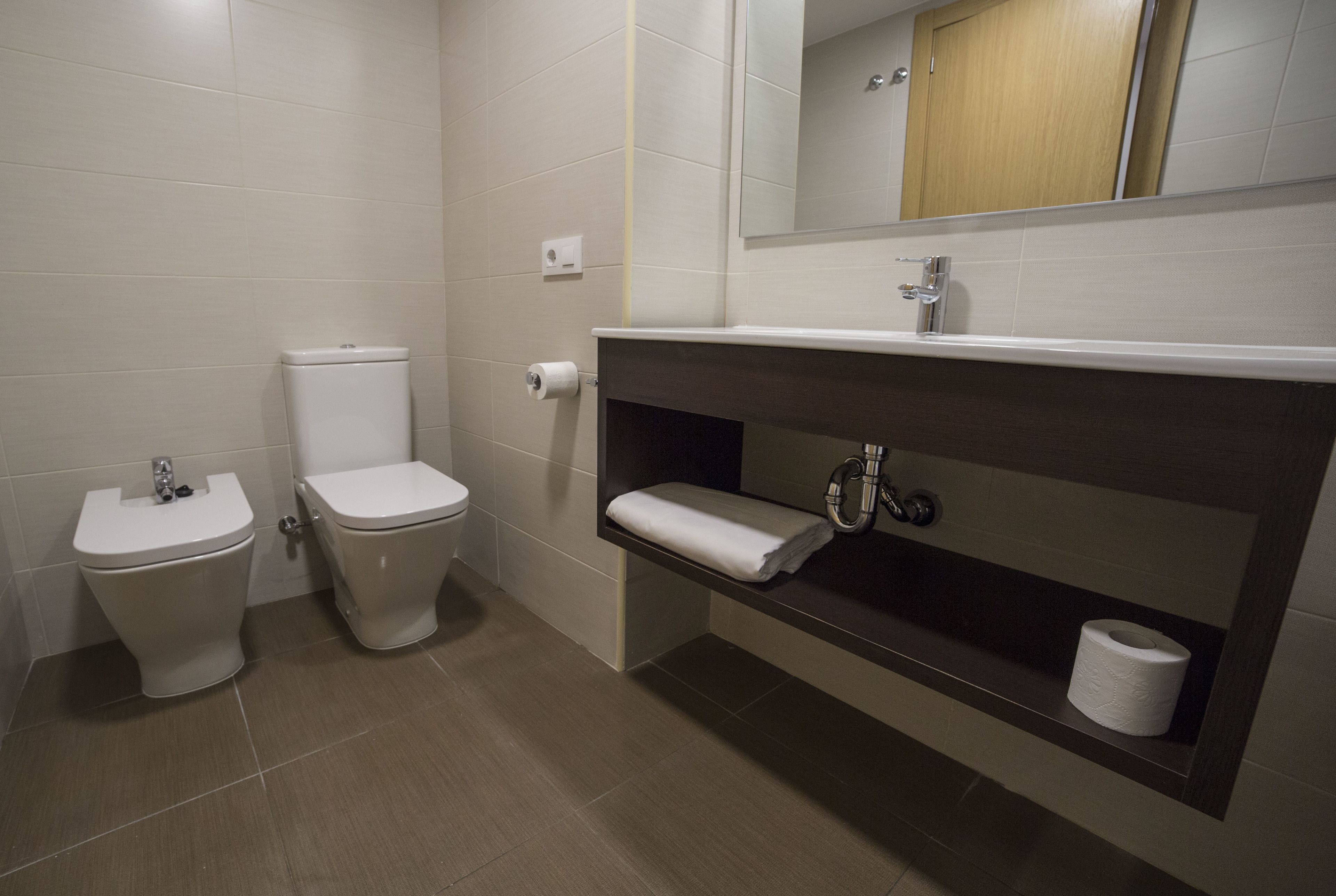 A modern bathroom with two toilets, a sink, and a mirror.