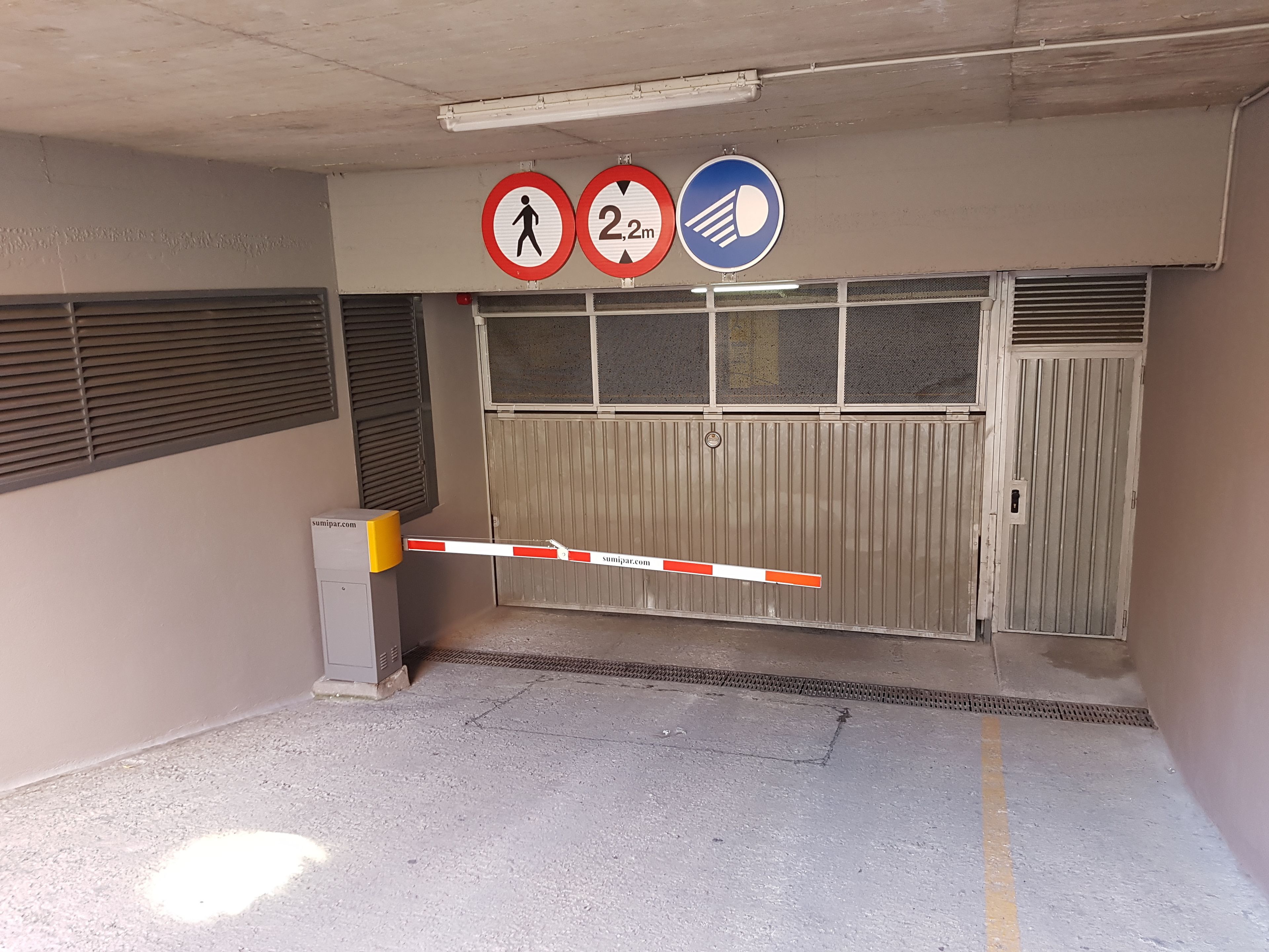 A gated entrance with a height restriction sign, a pedestrian crossing sign, and a no parking sign.