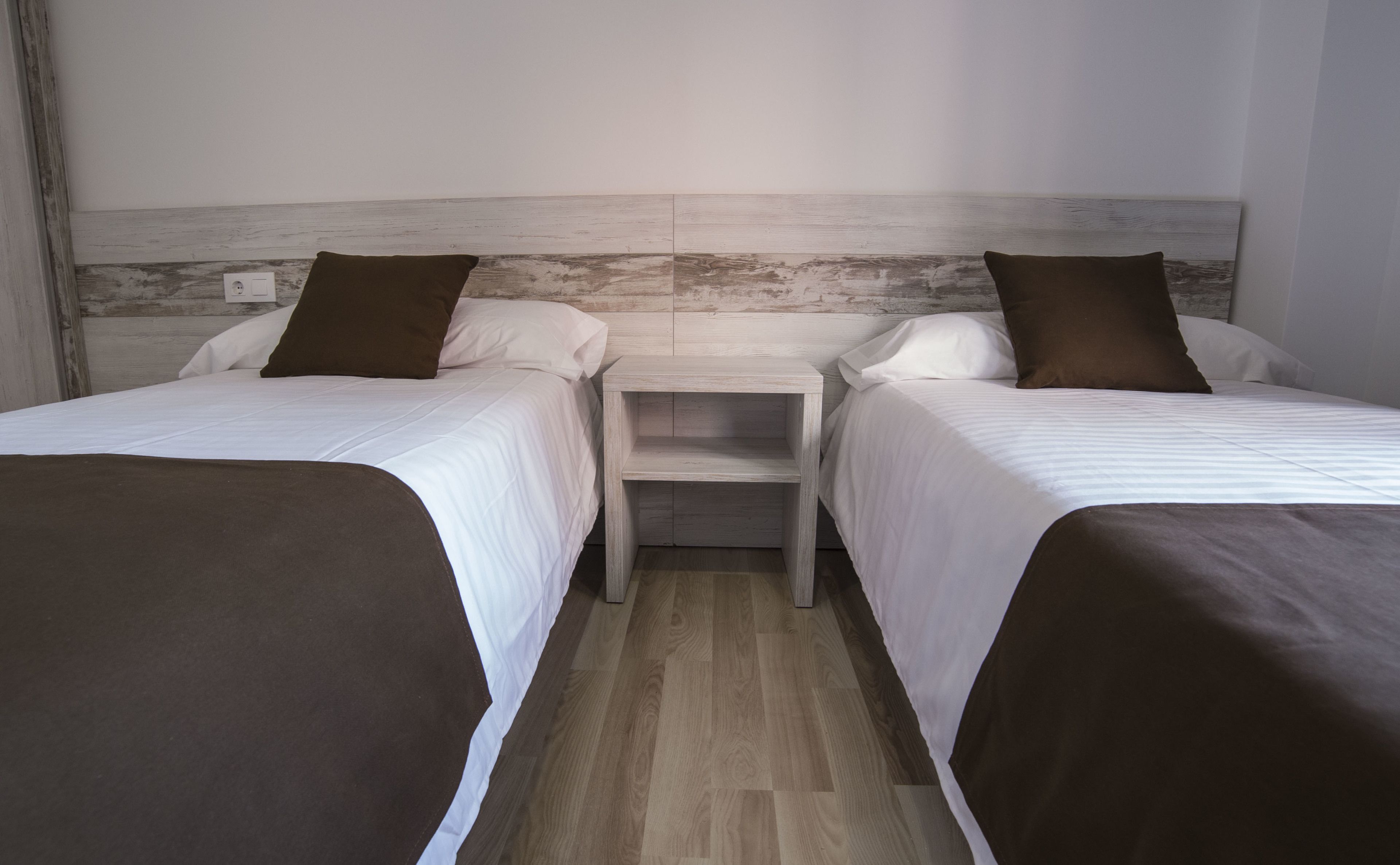 A hotel room with two beds, a wooden headboard, and a nightstand between them.
