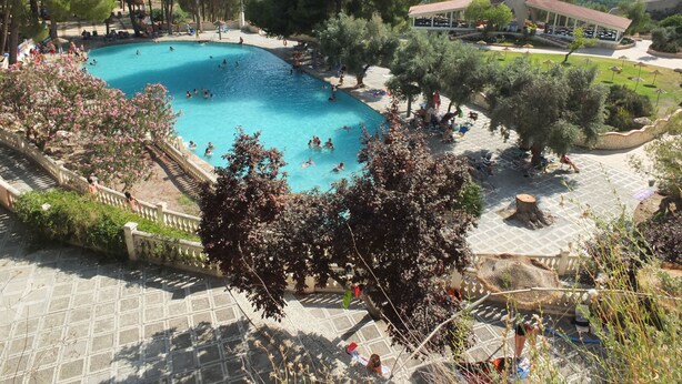A swimming pool surrounded by trees and a covered seating area. - Balneario de Alicún de las Torres (Villanueva de las Torres)