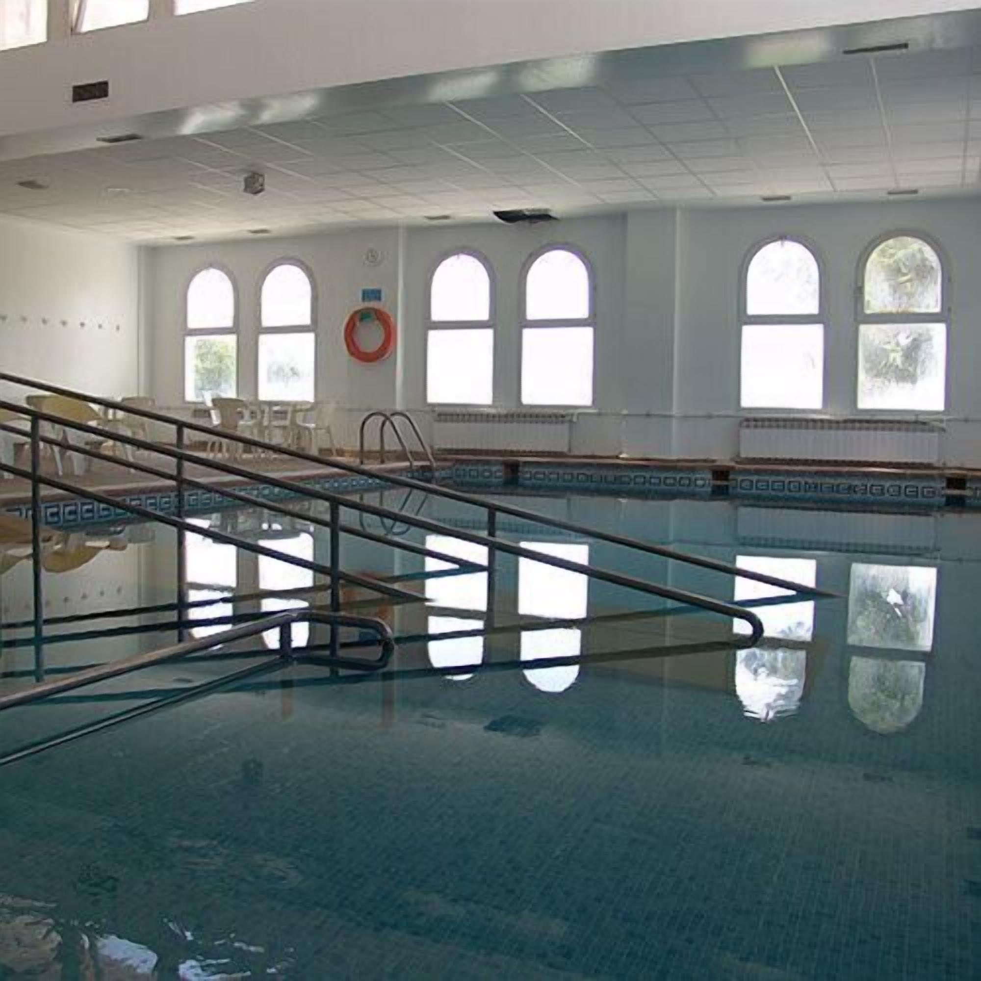 Una piscina interna con pareti di vetro trasparenti, una scala in metallo e un galleggiante appeso al muro.