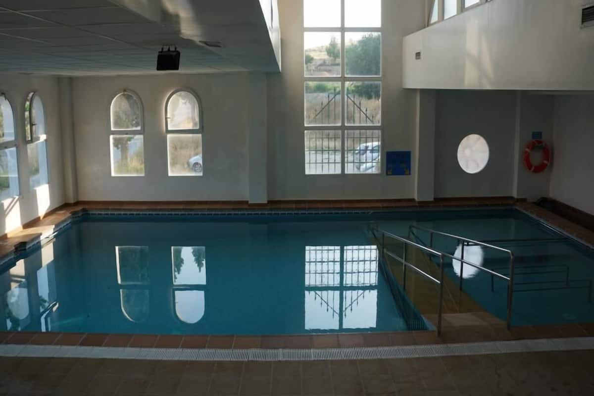 An indoor swimming pool with clear glass walls, large windows, and a lifebuoy on the wall.