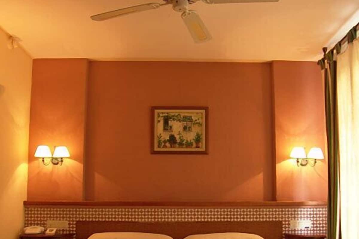 A hotel room with two beds, a ceiling fan, wall-mounted lamps, and a framed picture on the wall.