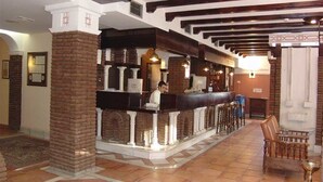 A lobby with a reception desk, a bar area, and a seating area with a chair and a lamp. - Balneario de Alicún de las Torres (Villanueva de las Torres)