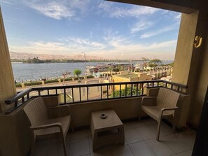 A balcony with two wicker chairs and a small table, overlooking a waterfront with buildings and a clear sky. - Luxor Hotel Armed Forces (Luxor)