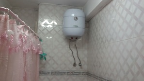A bathroom with a white water heater mounted on the wall, a pink shower curtain, and patterned tiles. - Luxor Hotel Armed Forces (Luxor)