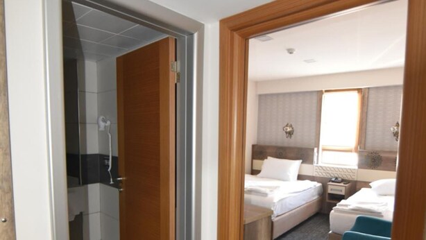 A hotel room with a shower, two beds, a desk, and a window. - Saltuk Otel (Erzurum)