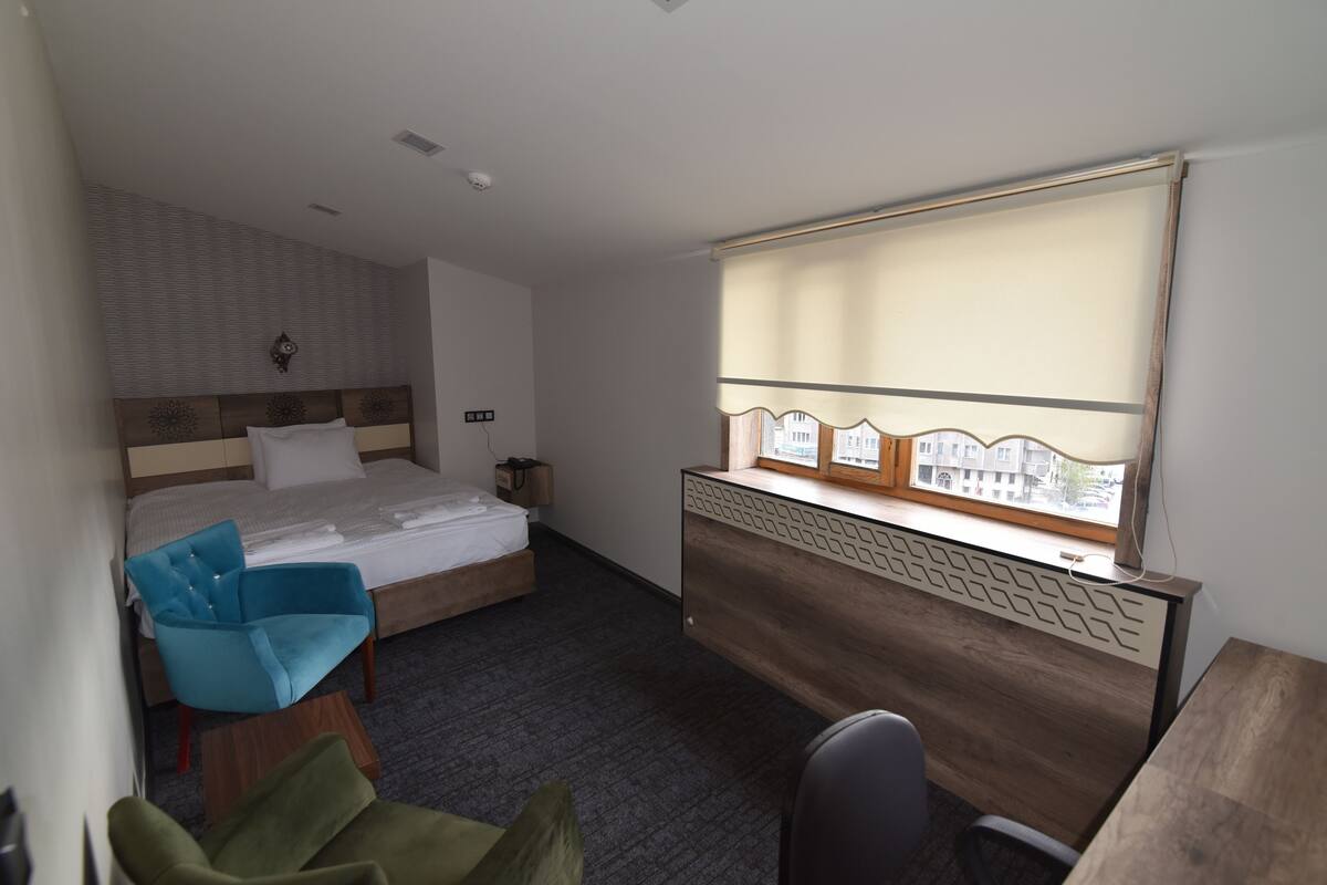 A hotel room with a bed, a desk, a chair, and a window with a view of buildings.
