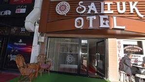 A hotel entrance with a sign reading "SAIUK HOTEL" and a PlayStation logo. There are chairs outside and a person sitting inside. - Saltuk Otel (Erzurum)