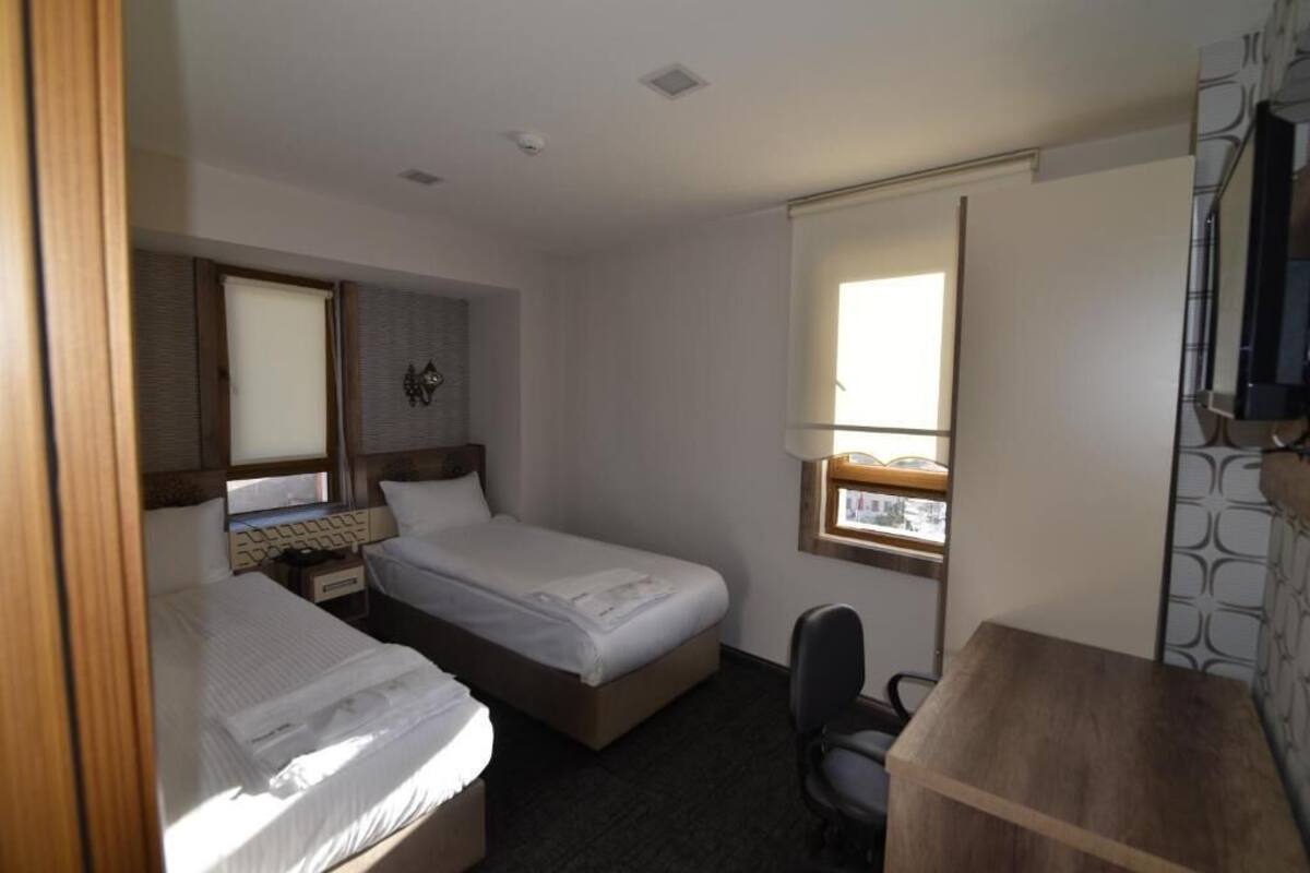 A hotel room with two single beds, a desk with a chair, a large mirror, and a window.