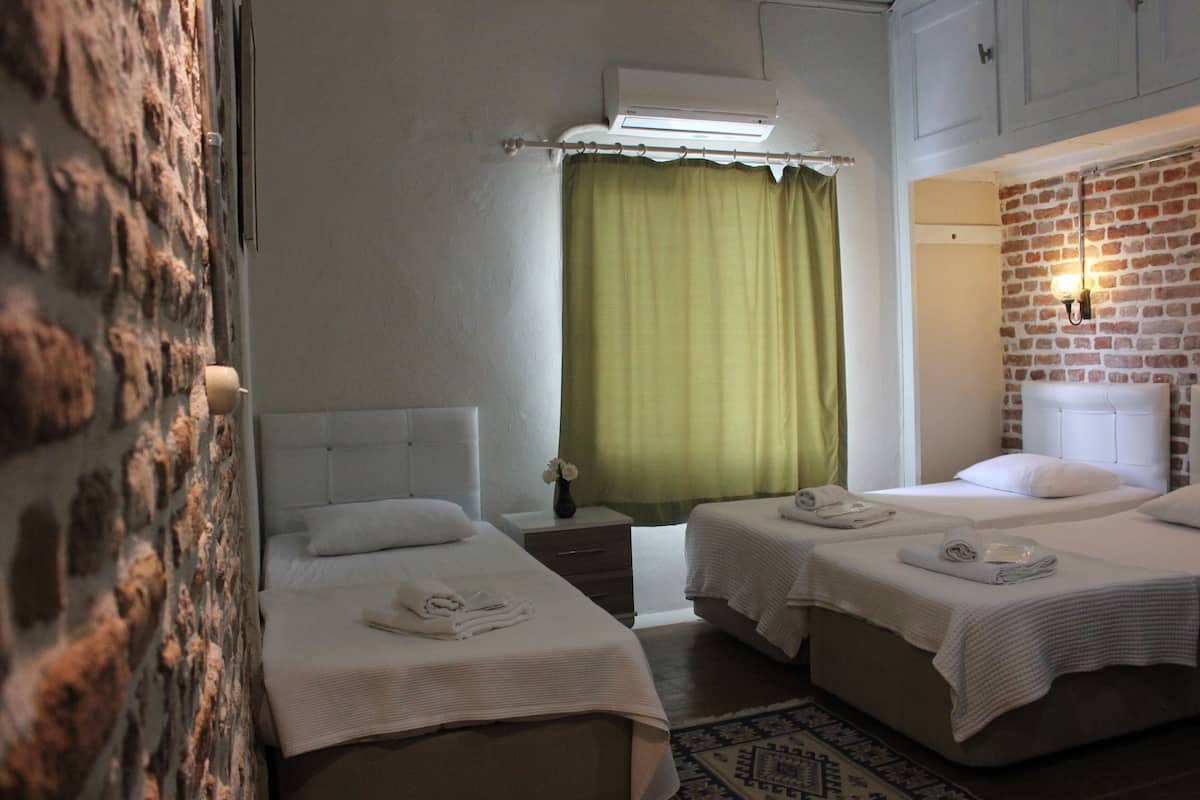 A hotel room with two beds, a brick wall, a green curtain, and a small table with a vase.