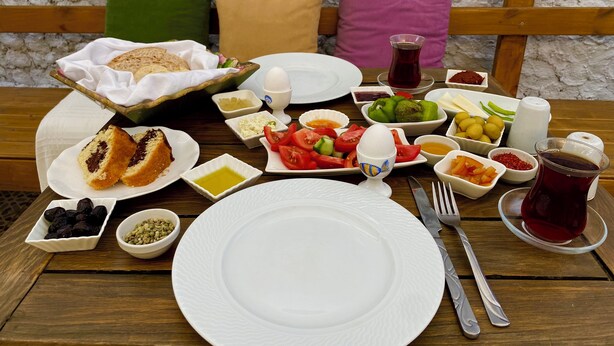 A table set with a variety of dishes, including bread, eggs, vegetables, and olives, with a wooden bench and cushions in the background. - Macide Hanim Konagi (Ayvalik)