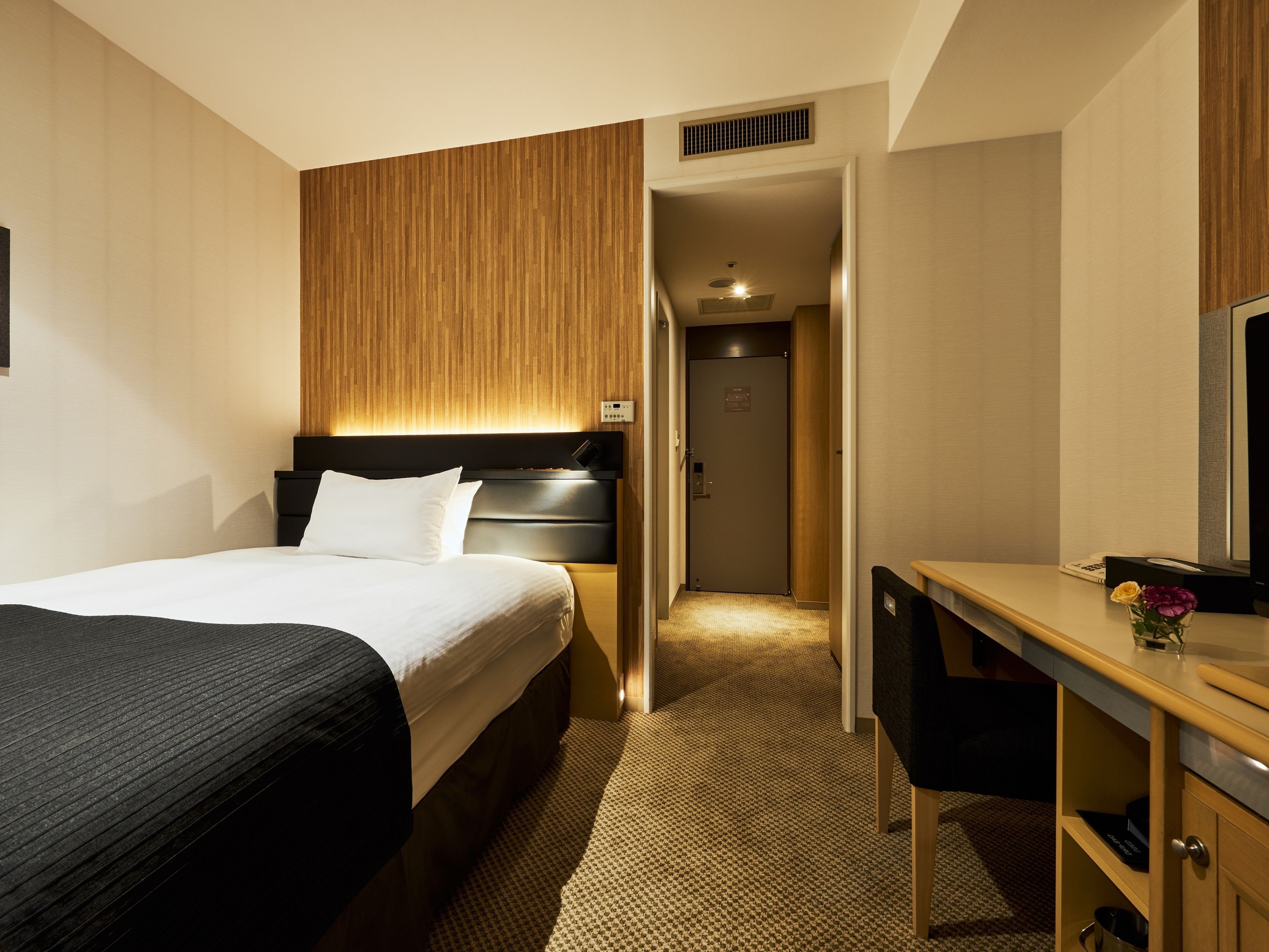 A hotel room with a bed, a desk, and a wardrobe.