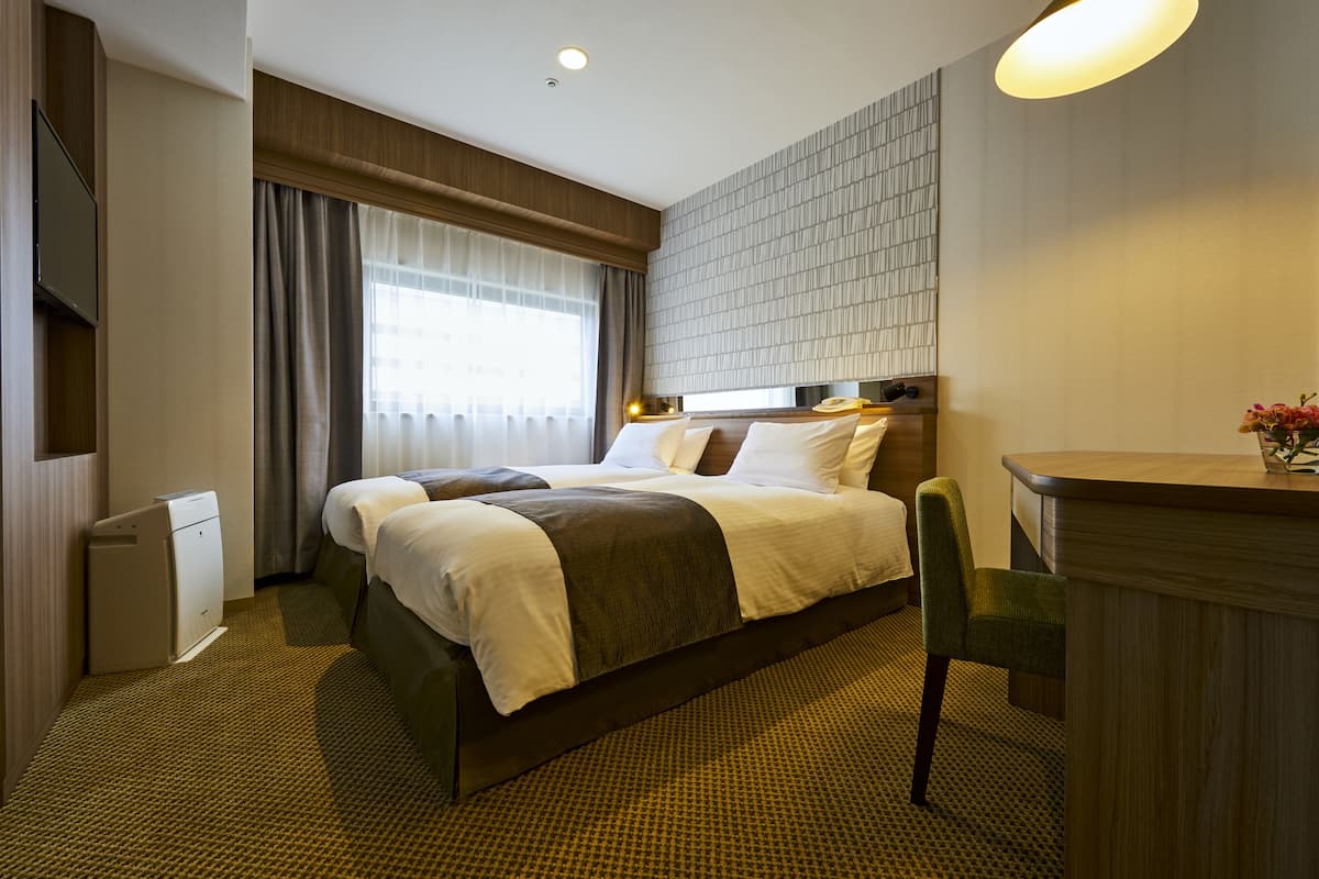 Une chambre d’hôtel avec un lit, un bureau, une chaise, une télévision et une fenêtre avec des rideaux.