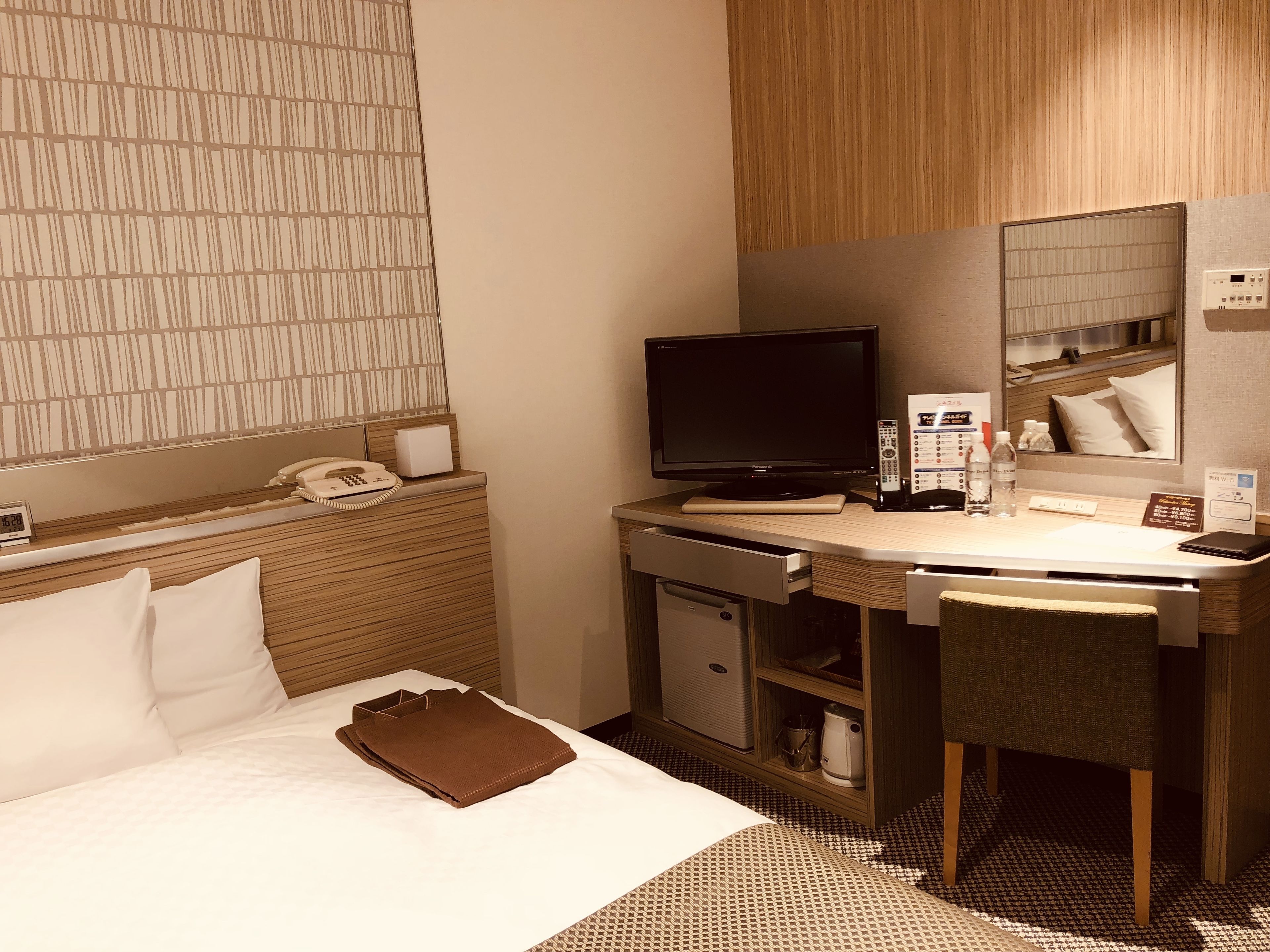 A hotel room with a bed, a desk with a computer, a telephone, and a mirror.