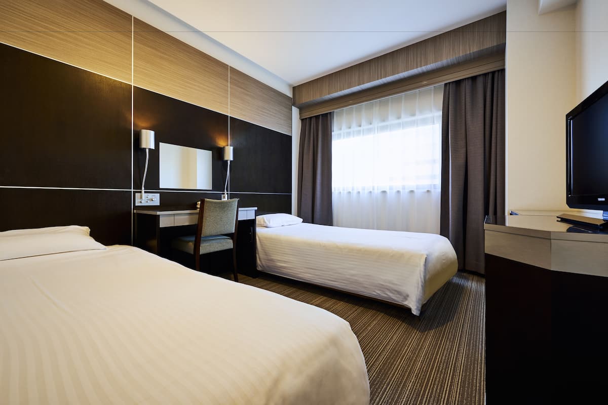 Une chambre d’hôtel avec deux lits, un bureau, une chaise, une télévision et une grande fenêtre avec des rideaux.