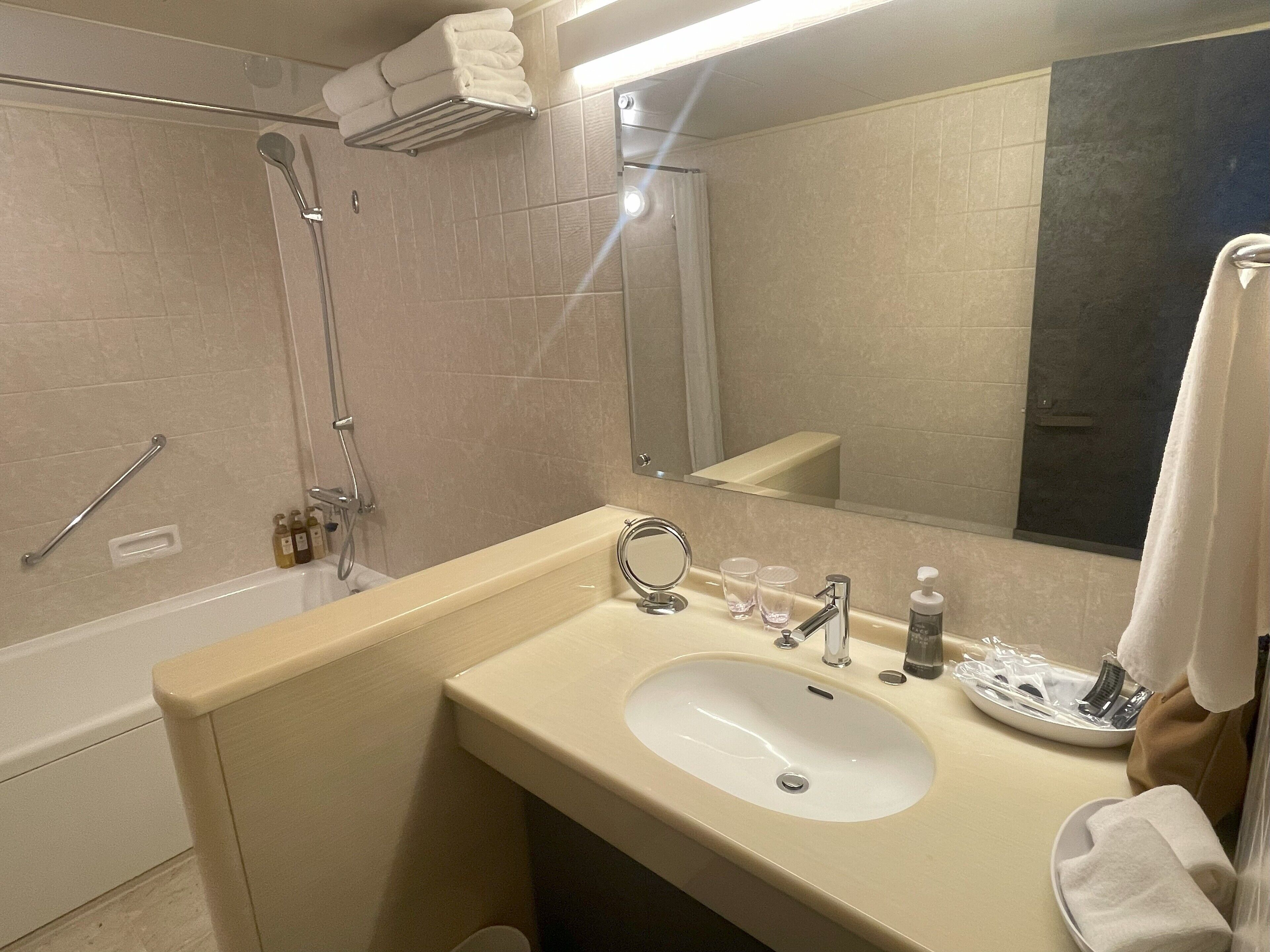 A bathroom with a sink, mirror, towel rack, shower, and a hand dryer.