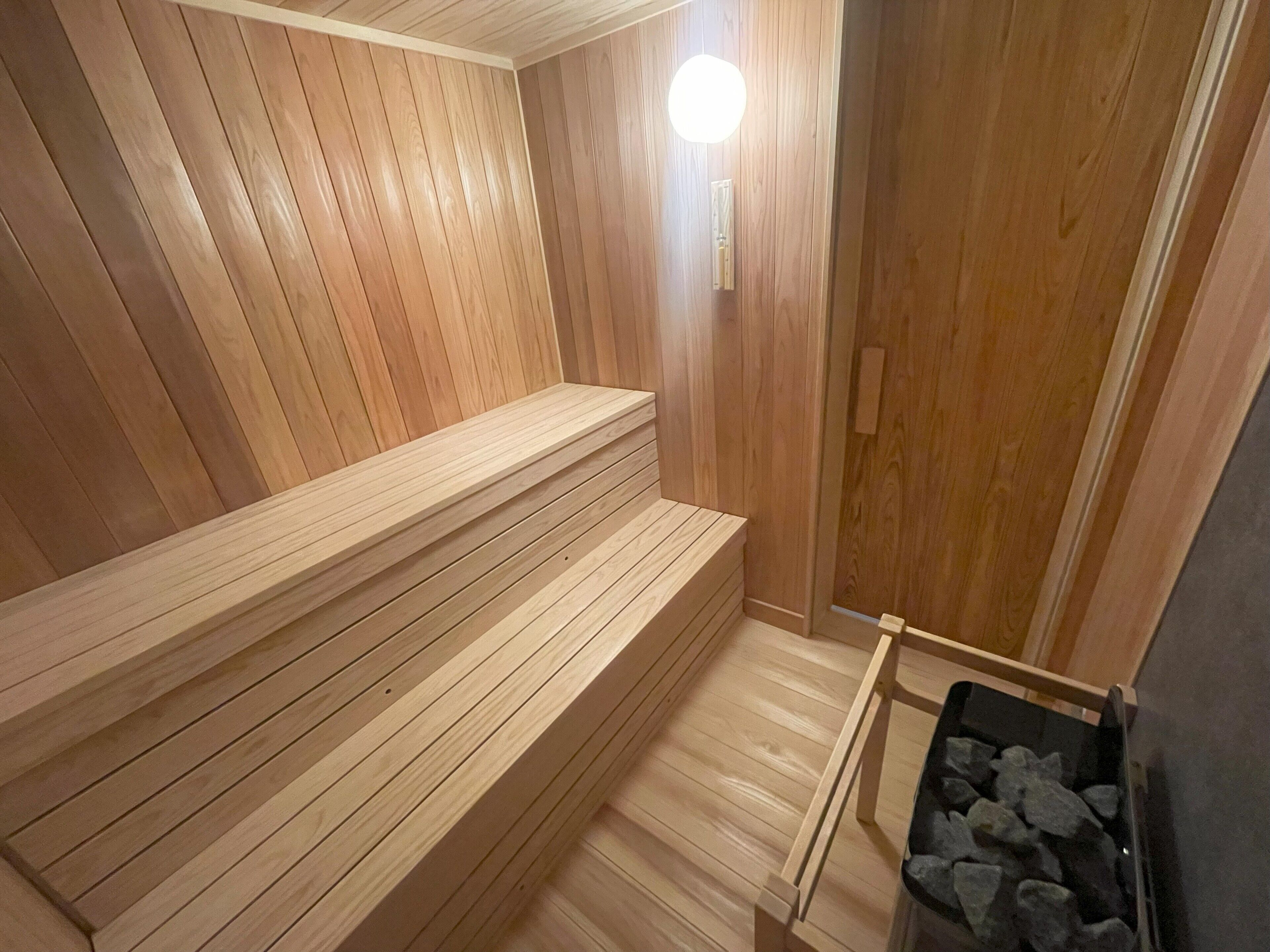 A wooden sauna with benches and a sauna table, a stone bench, and a sauna heater.