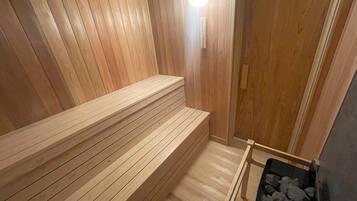 A wooden sauna with benches and a sauna table, a stone bench, and a sauna heater.