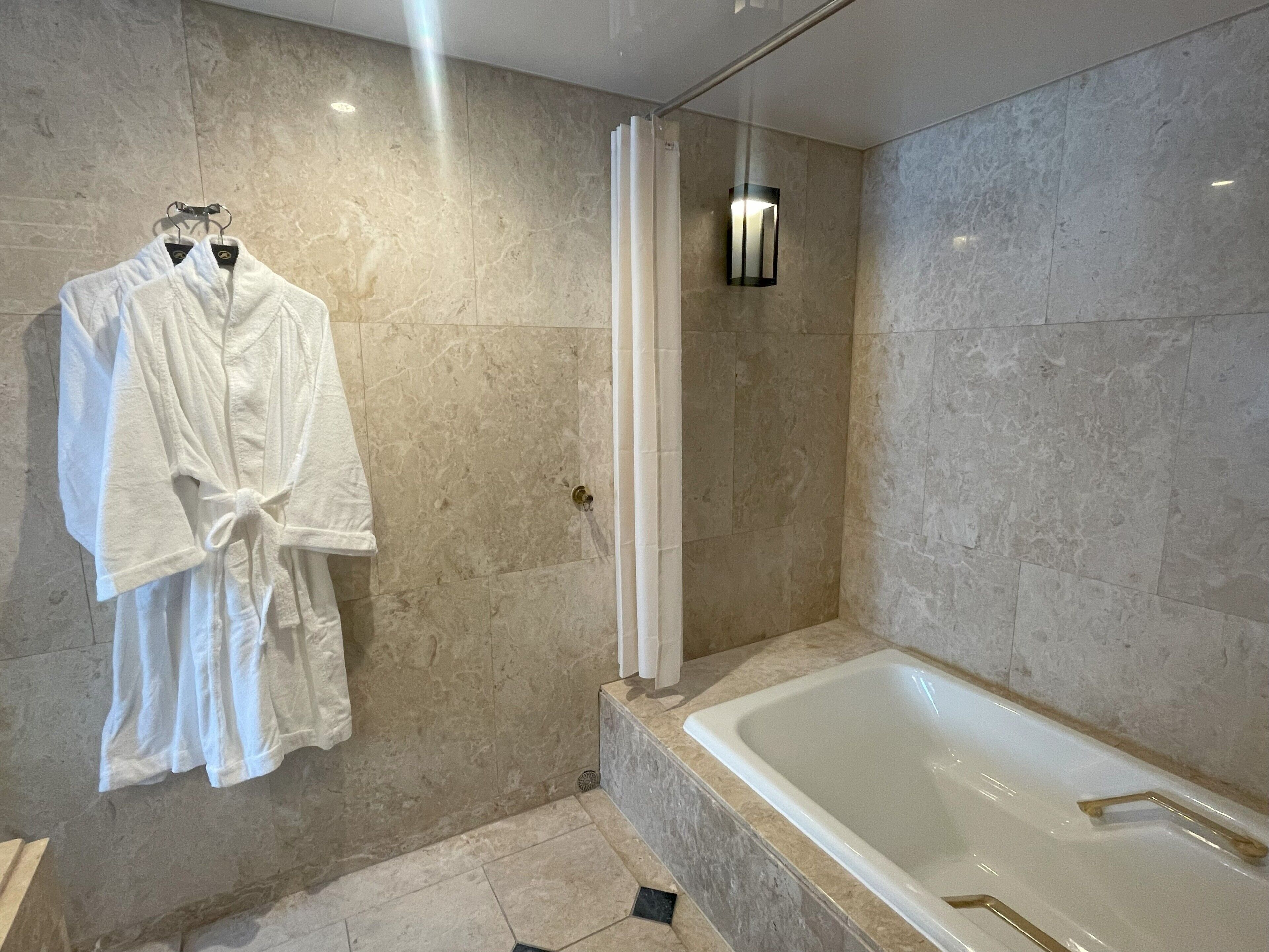 Un baño moderno con bañera, cortina de ducha y dos albornoces blancos colgados en un perchero.