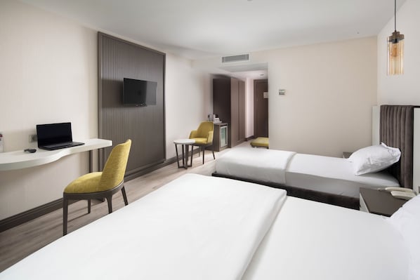 A hotel room with two beds, a desk with a laptop, a chair, and a television.