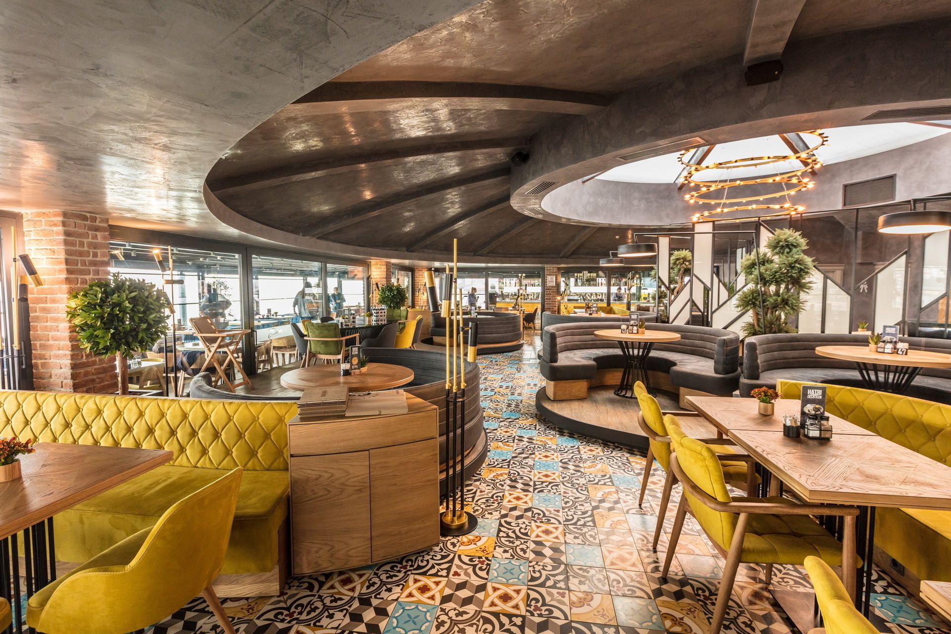 Interior moderno de restaurante con techo curvo, paredes de ladrillo visto y una variedad de opciones de asientos, incluyendo cabinas y mesas.
