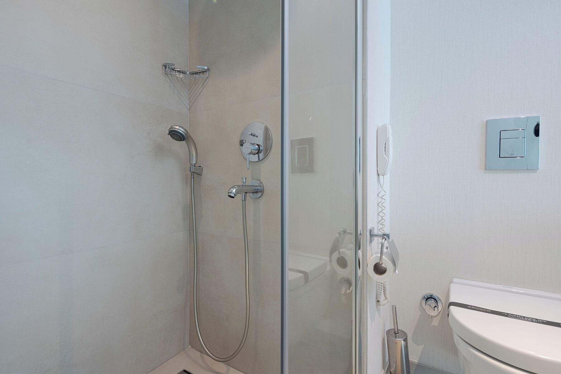 A modern bathroom with a glass shower enclosure, a toilet, and a wall-mounted telephone.
