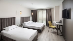 Une chambre d’hôtel avec deux lits, un bureau, une chaise, une télévision et un balcon avec des rideaux.