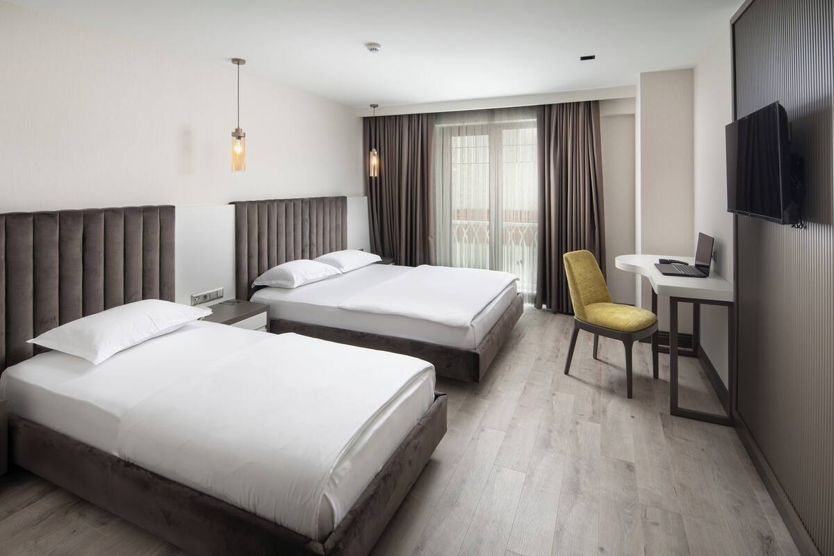 Habitación de hotel con dos camas, un escritorio, una silla, un televisor y un balcón con cortinas.