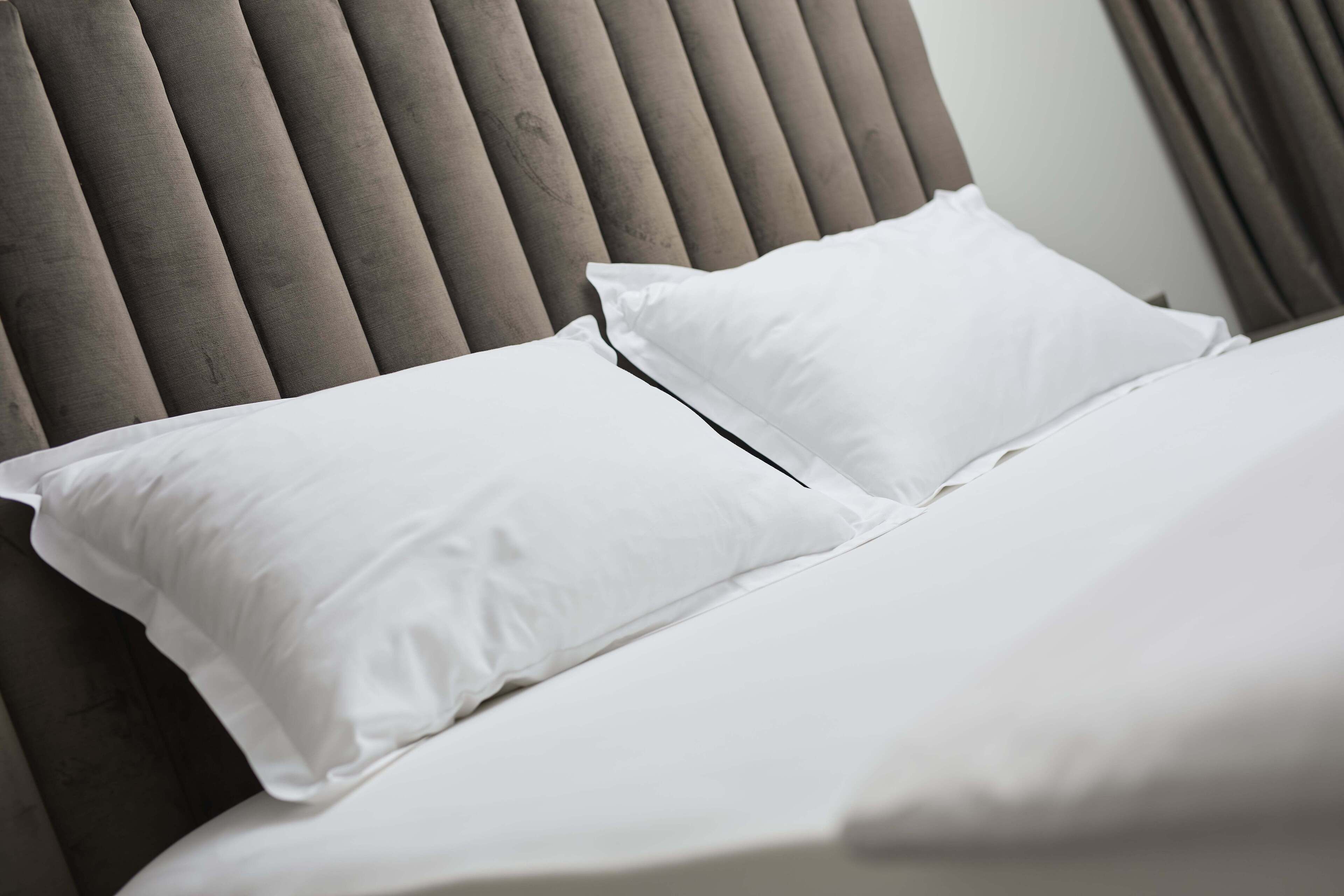 A bed with white bedding and a grey upholstered headboard.