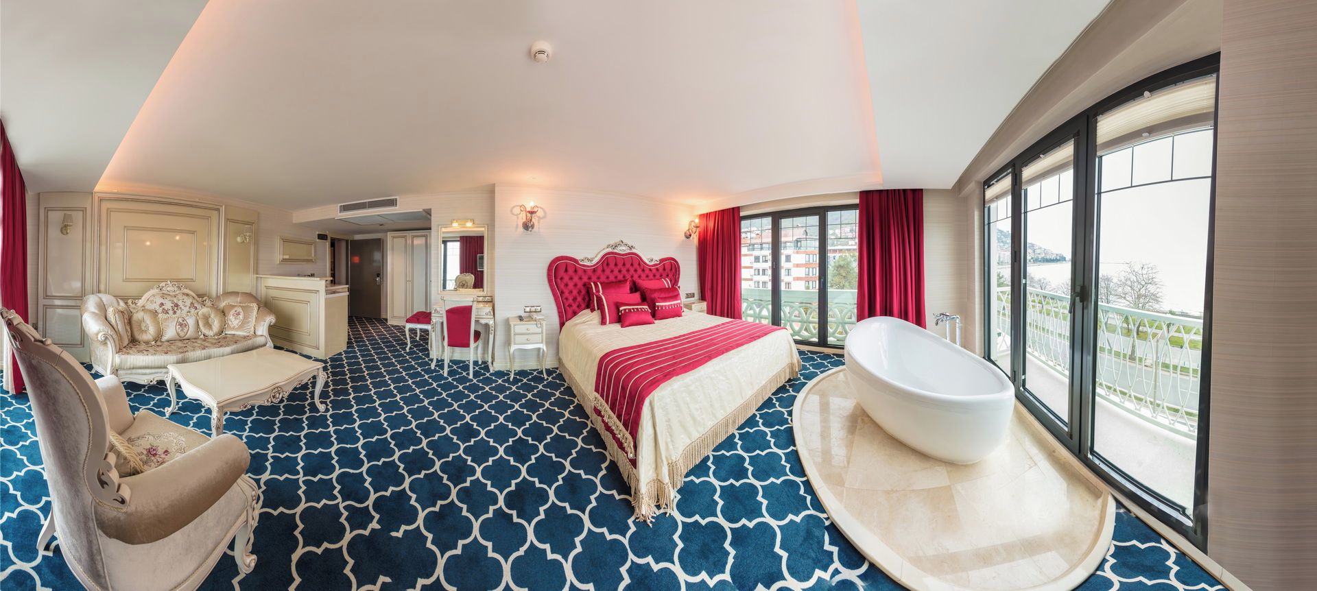 Habitación de hotel con una cama grande, una zona de estar con sofá y sillón, un escritorio y una bañera.