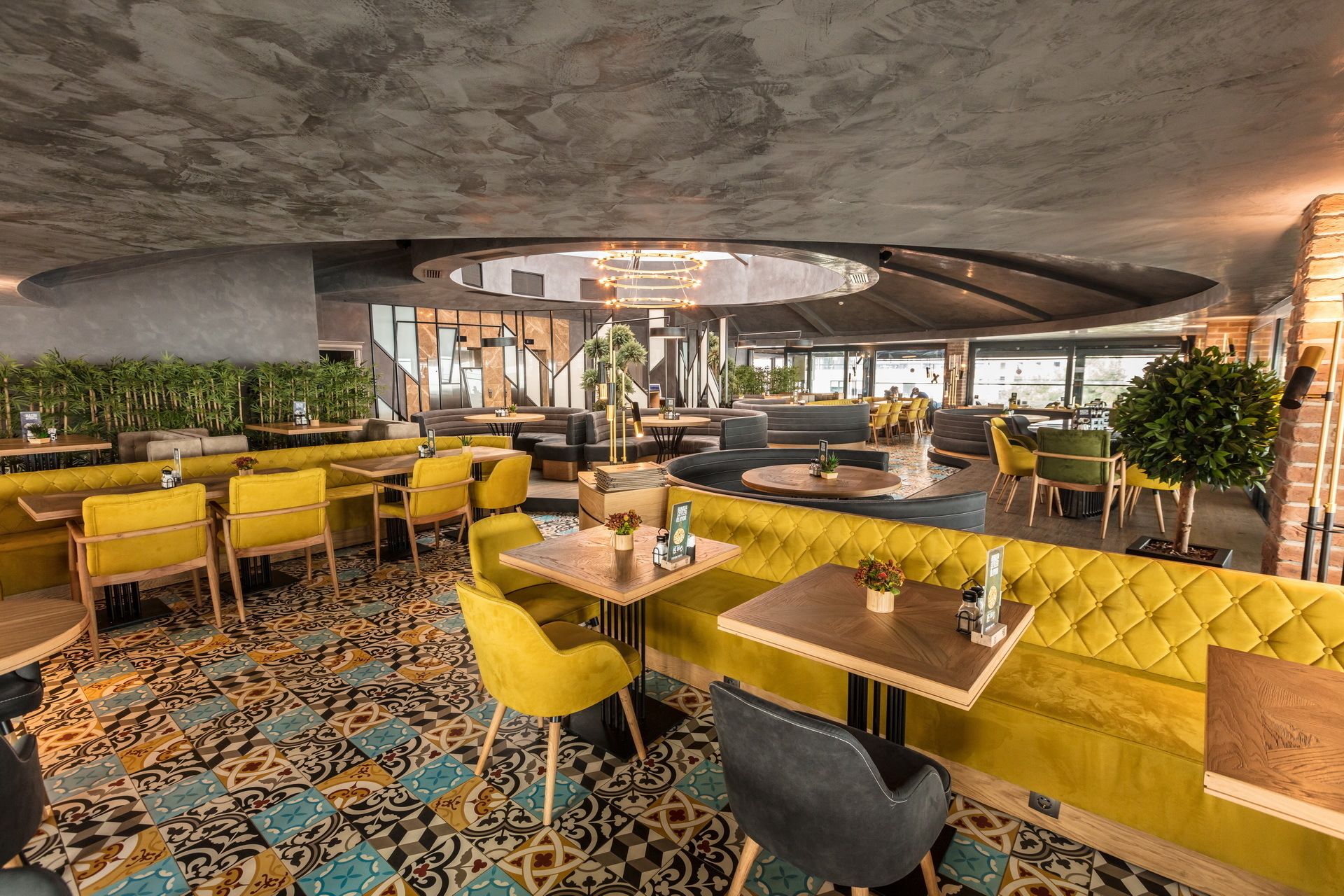Un ristorante moderno con sedute gialle e grigie, piastrelle decorative e una zona pranzo centrale circolare.