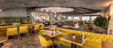 Un restaurante moderno con asientos amarillos y grises, baldosas de suelo estampadas y una zona de comedor circular central.