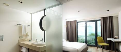 Una habitación de hotel con baño, cama, escritorio y vistas al exterior.