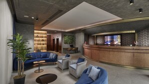 Un hall d’entrée moderne avec un comptoir d’accueil incurvé, un espace salon avec des canapés et des fauteuils, et une grande plante en pot.
