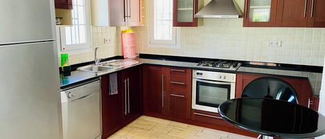 A modern kitchen with wooden cabinets, a stainless steel refrigerator, a gas stove, and a dishwasher.