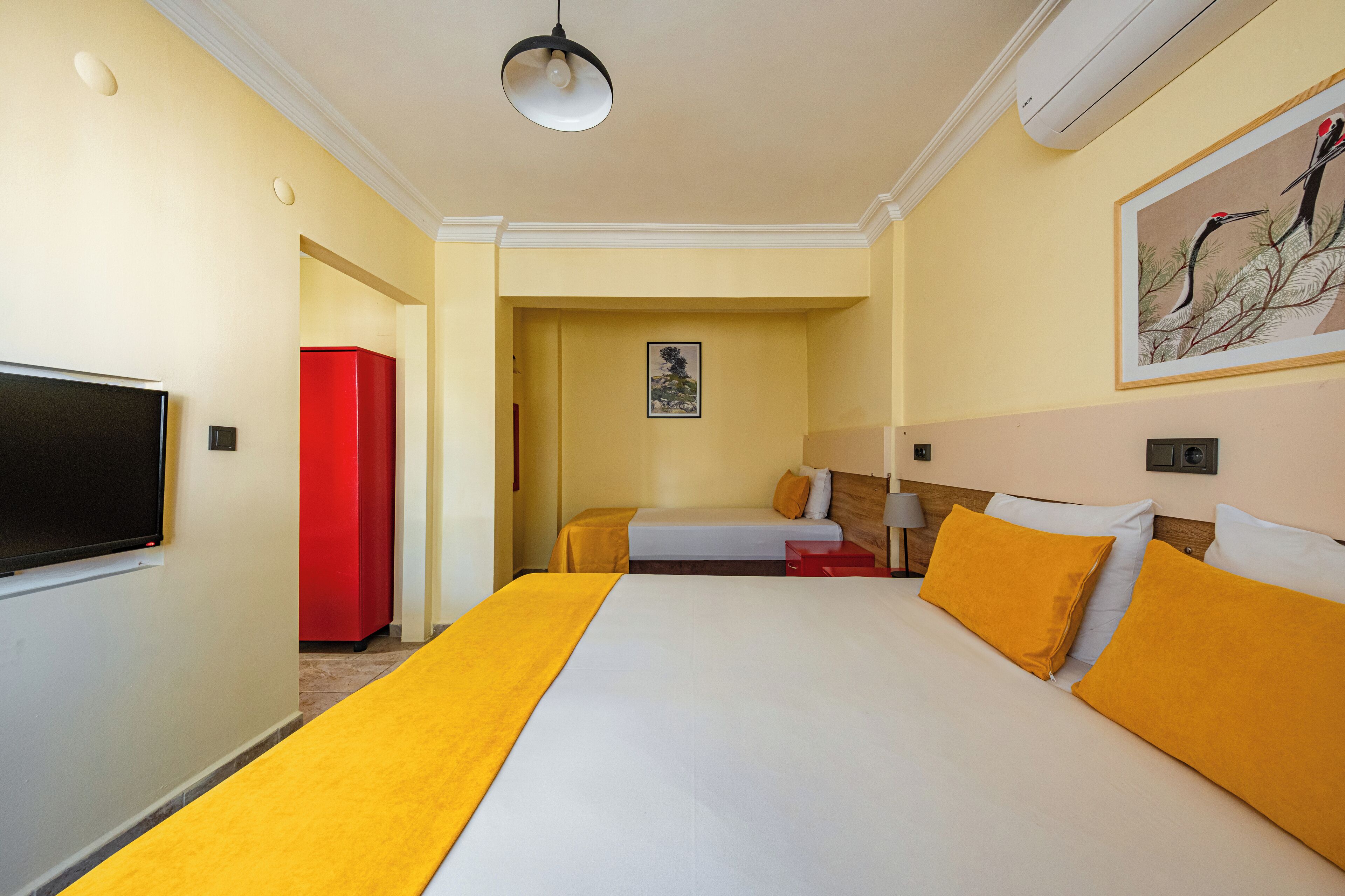 A hotel room with a large bed, a television, a red cabinet, and a painting on the wall.