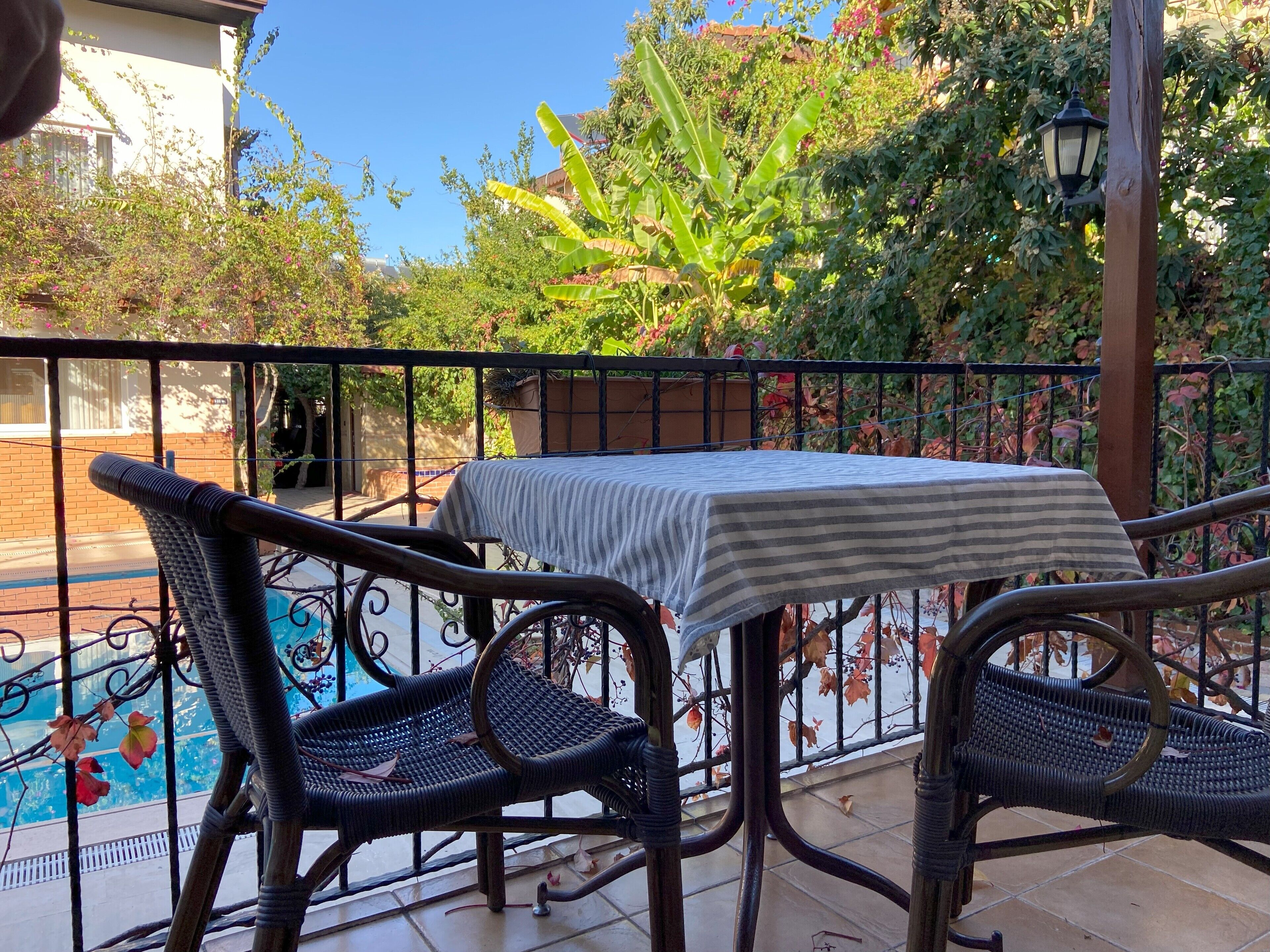 Un balcon avec une table et des chaises, une piscine et de la verdure tout autour.