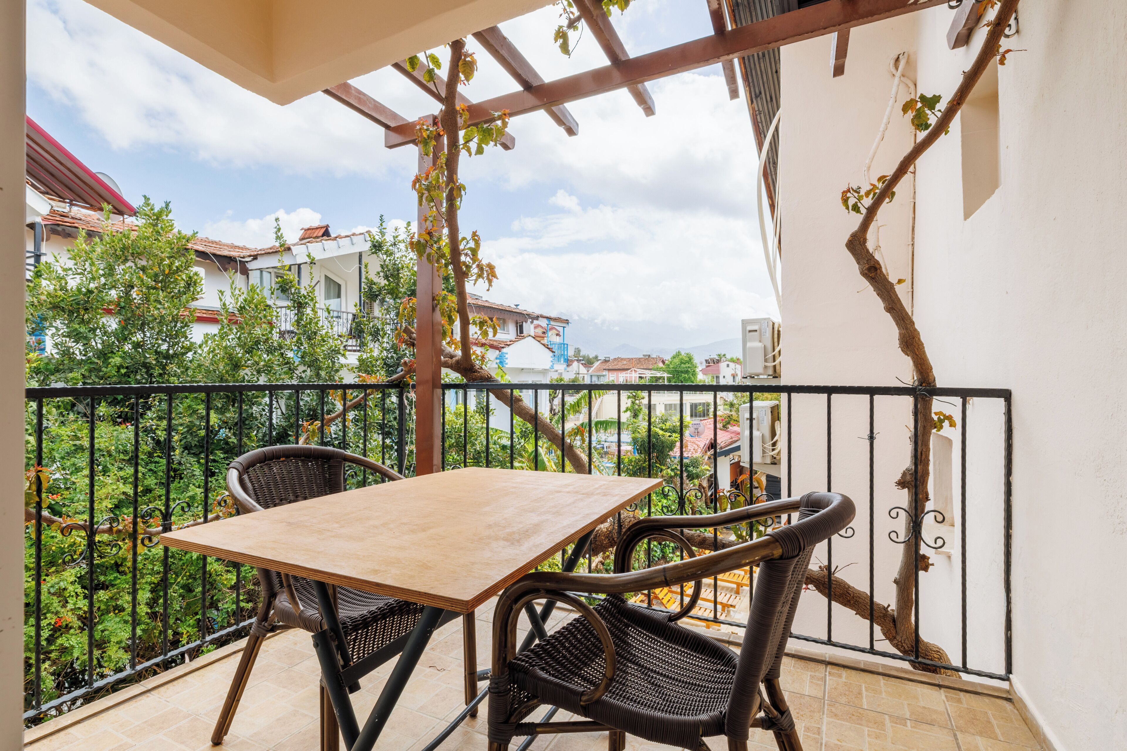 Un balcon avec une table et des chaises, une vue sur le quartier et une structure en forme de pergola.