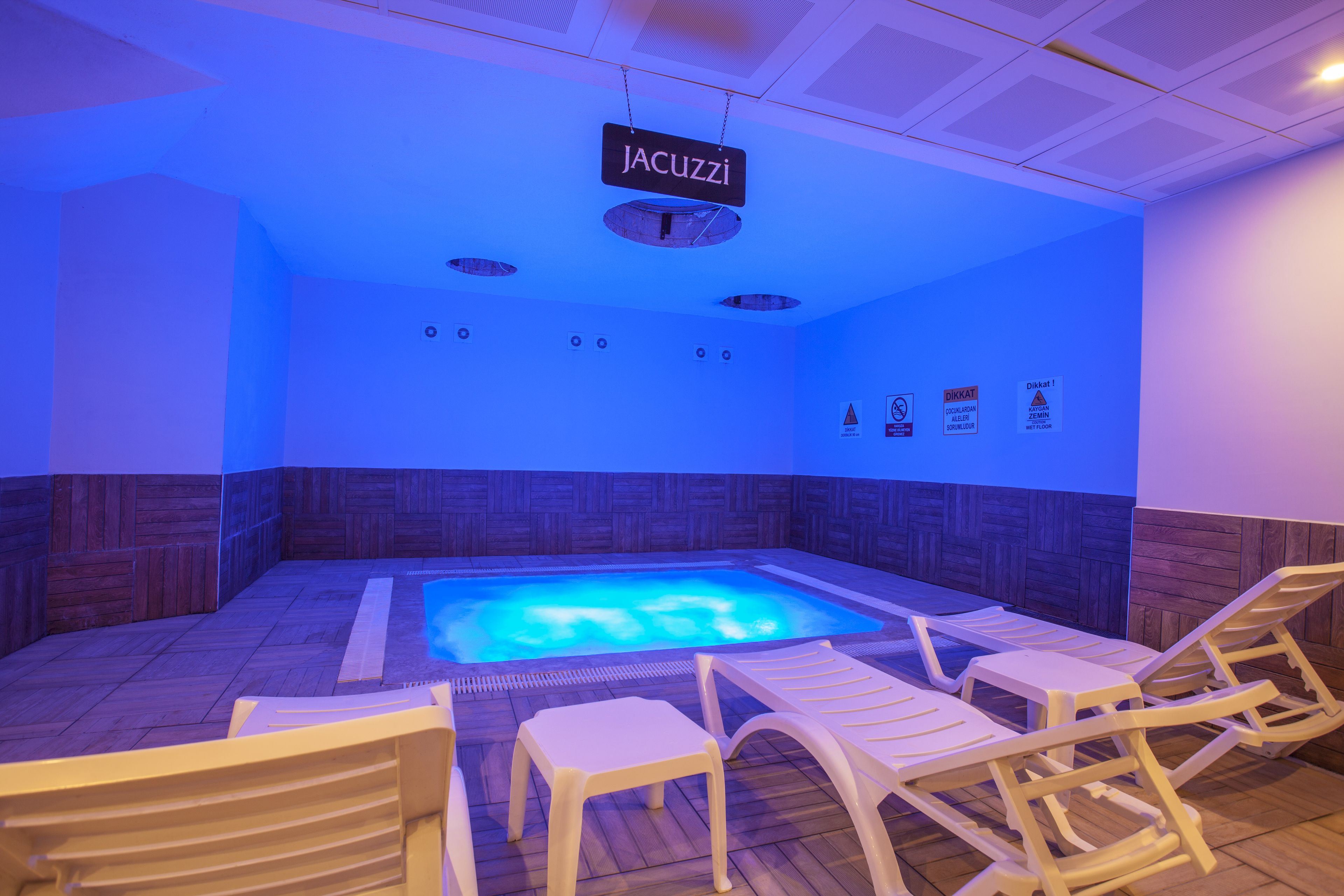 Zona de piscina interior climatizada con sillones de descanso y un letrero que dice 'JACUZZI'.