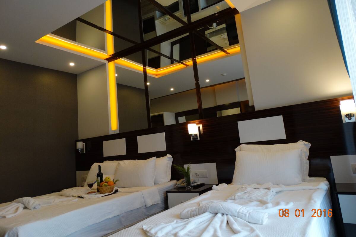 Een hotelkamer met twee bedden, een grote spiegel en een modern plafondontwerp.