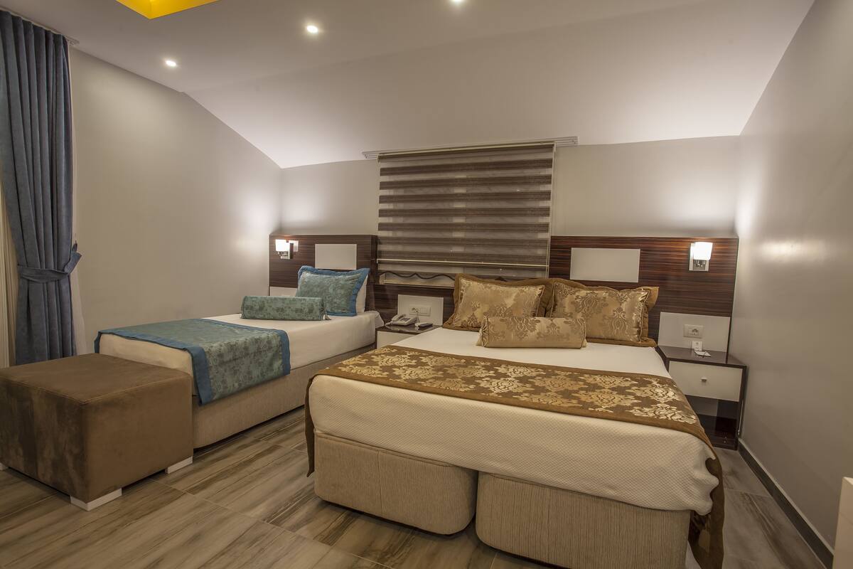 Een moderne slaapkamer met twee bedden, een groot raam met zonwering, bedlampen en een klein tafeltje met een telefoon.