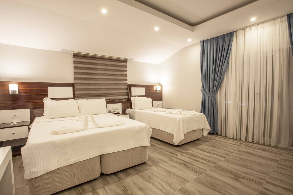 Een moderne hotelkamer met twee bedden, houten hoofdborden, nachtkastjes en een grote kledingkast met gordijnen.