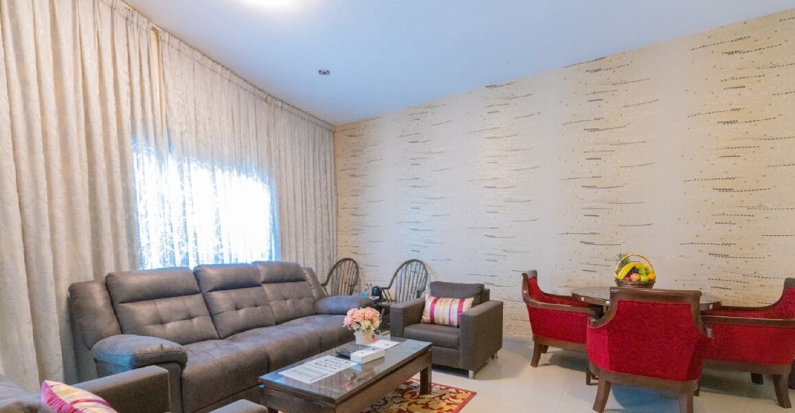 A living room with a sofa, armchairs, a coffee table, and a small table with a fruit bowl.