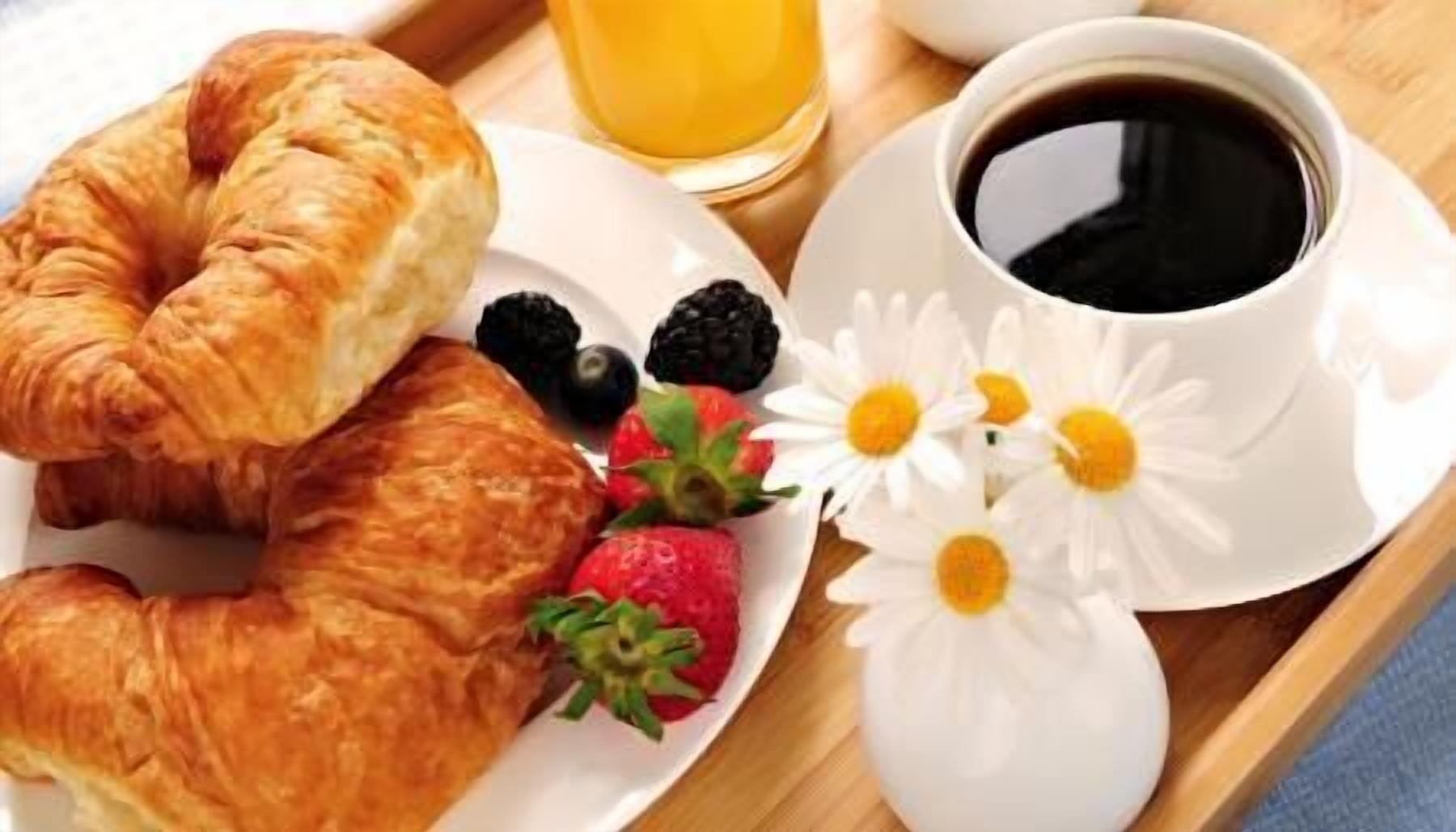 Bandeja de desayuno con cruasanes, fresas, zarzamoras, un vaso de jugo de naranja y una taza de café.