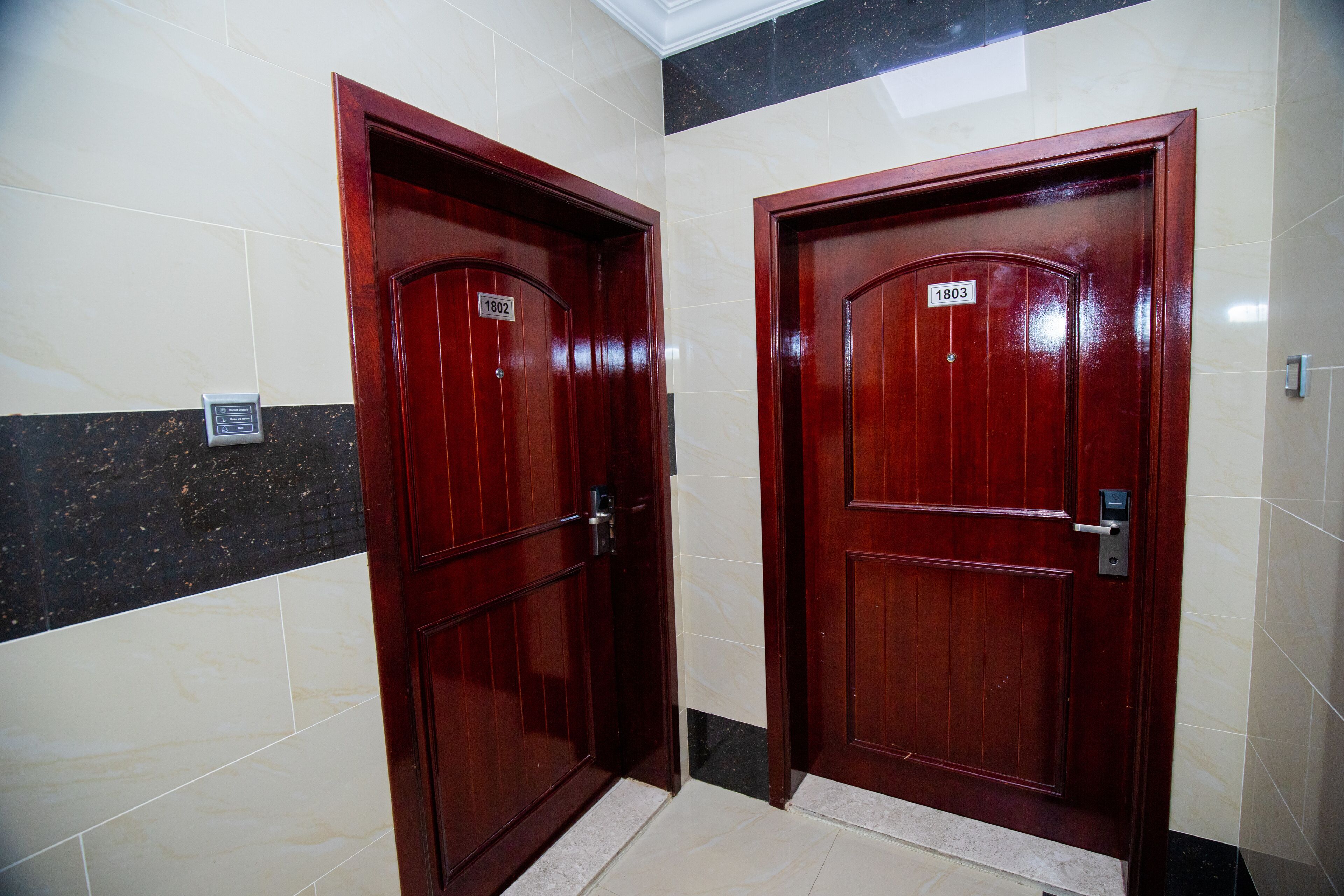 Two wooden doors with numbers 1802 and 1803, indicating room numbers, in a hallway with tiled walls and a marble floor.