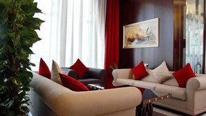 Una sala moderna con dos sofás, cojines rojos, una planta grande y un cuadro en la pared.