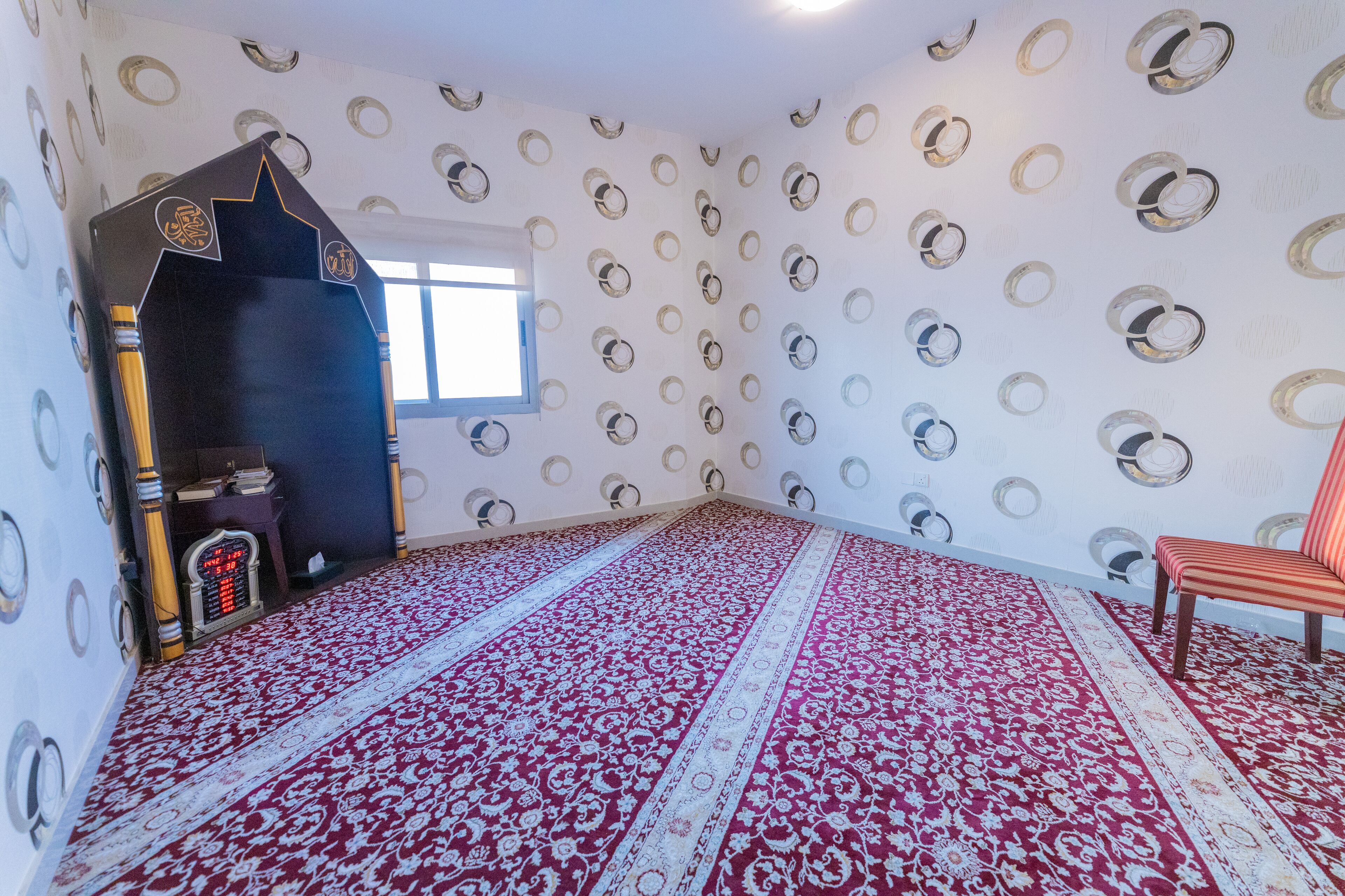 A room with a patterned carpet, a star-shaped door, a window, and a chair.