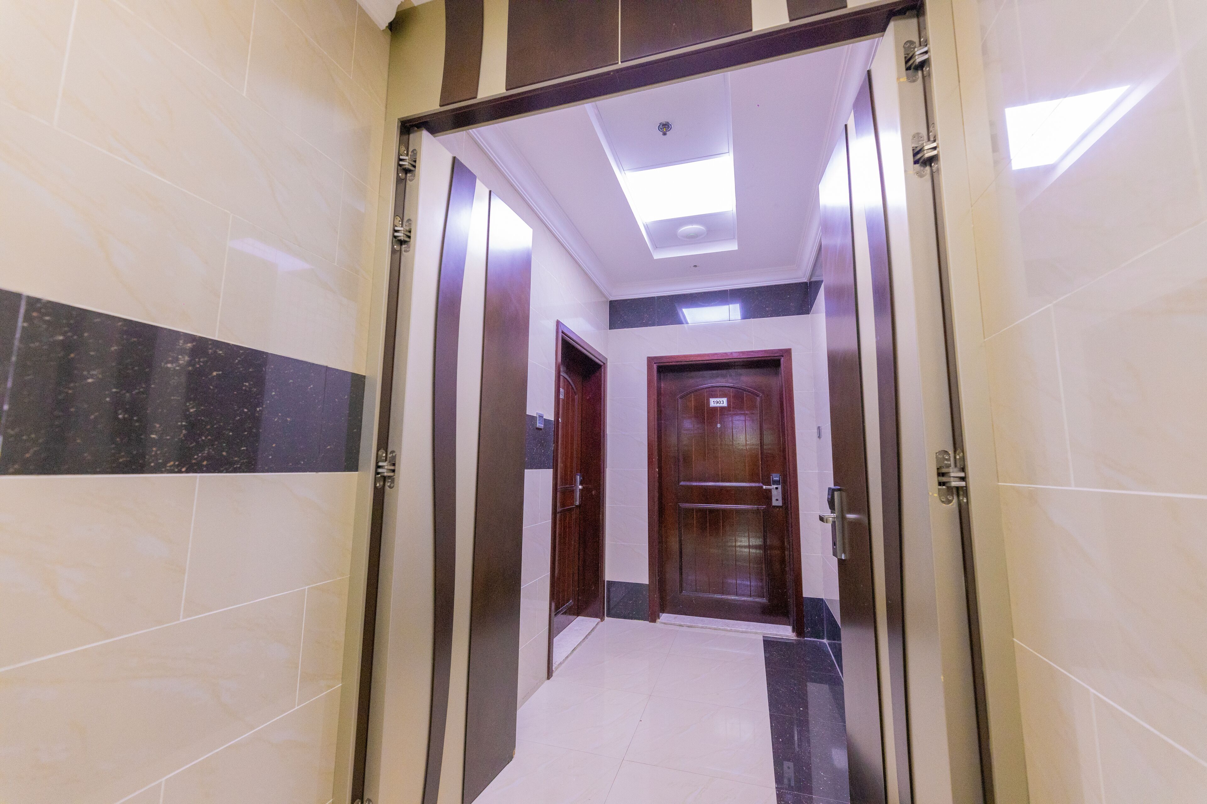 A hallway with a tiled floor, a wooden door, and a ceiling light.